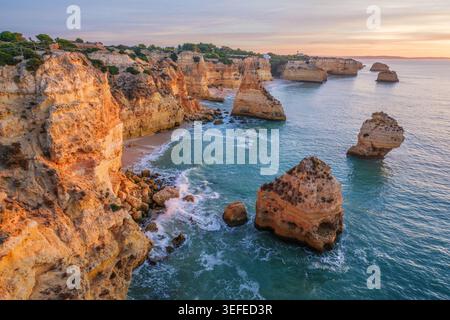 Blick auf den Strand Praia da Marinha in der Algarve, Portugal, mit einem Meeresbogen aus Kalkstein, Atlantikwasser, warmem Himmel und zerklüfteten Küstenklippen. Stockfoto