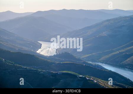 Der Blick auf die Drohne fängt den Sonnenaufgang über dem Flusskorridor des Douro-Tals in Portugal ein. Weinberge umgeben die Gegend, mit einem Touristenboot, das entlang fährt Stockfoto