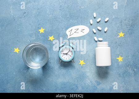 Wecker mit einem Glas weißer Pillen, Papiersternen und einem Glas Wasser auf blauem Hintergrund Stockfoto