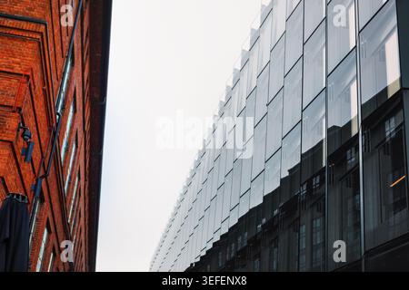 Ein markanter architektonischer Kontrast zeigt ein Gebäude aus rotem Backstein und eine moderne Glasverkleidung. Gegenüberstellung hebt die Entwicklung der Stadt hervor Stockfoto