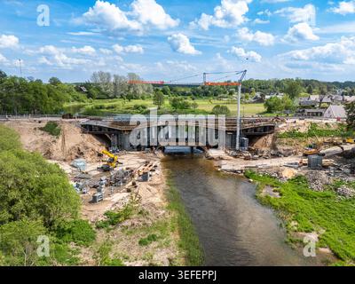 Aus der Vogelperspektive des Wiederaufbaus einer Brücke über einem Fluss im ländlichen Litauen mit Kranichen, Gerüsten und Baustellen in der Nähe einer kleinen Stadt während der Frühlingszeit. Stockfoto