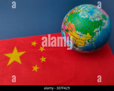 Ein kleiner Globus, der Asien zeigt, befindet sich auf der rechten Seite einer chinesischen Flagge. Stockfoto