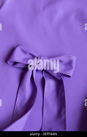 Eine Nahansicht zeigt eine Schleife aus violettem Stoff, die auf einem glatten Hintergrund platziert ist. Das Licht betont die Textur und Falten des verwendeten Materials. Stockfoto