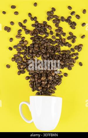 Kaffeebohnen kommen aus einer Tasse vor einem gelben Hintergrund Stockfoto