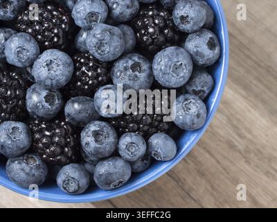 Schüssel voller frischer Brombeeren und Heidelbeeren auf hölzernem Hintergrund Stockfoto