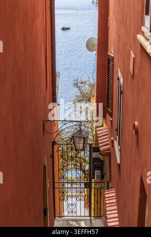 Malerischer Blick durch eine enge Straße in Positano, Italien, mit traditionellen Gebäuden, Vintage-Laterne und einem Blick auf den Strand und das türkisfarbene Meer Stockfoto