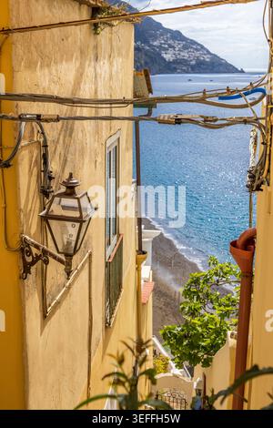 Malerischer Blick durch eine enge Straße in Positano, Italien, mit traditionellen Gebäuden, Vintage-Laterne und einem Blick auf den Strand und das türkisfarbene Meer Stockfoto