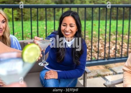 Verschiedene Gruppen glücklicher Frauen, die Getränke teilen und sich auf einer Terrasse unterhalten, ein geselliges Treffen genießen und die Freundschaft im Freien mit Getränken feiern. Stockfoto