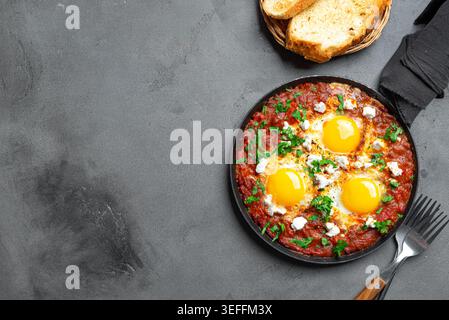 Shakshuka: Spiegeleier in würziger Tomatensauce, garniert mit Fetakäse und Petersilie. Shakshuka - mediterranes Helthy-Frühstück auf Betonhintergrund, Stockfoto