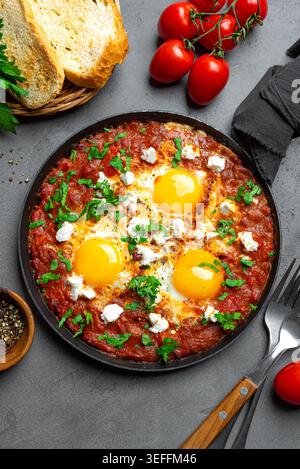 Shakshuka mit pochierten Eiern in würziger Tomatensauce, garniert mit Fetakäse und Petersilie in einer gusseisernen Pfanne. Shakshuka: Mediterranes Helthy-Frühstück. Stockfoto
