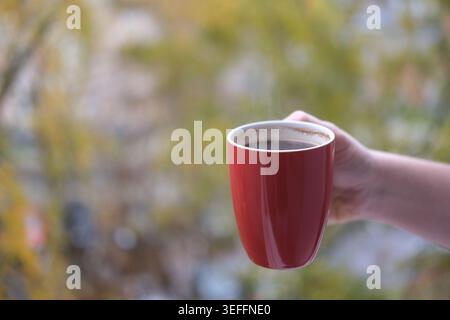 Rote Kaffeetasse in der Hand draußen Stockfoto