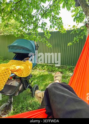 Entspannen Sie sich in der Hängematte in der Nähe des Kinderwagens im sonnigen Hinterhof Stockfoto