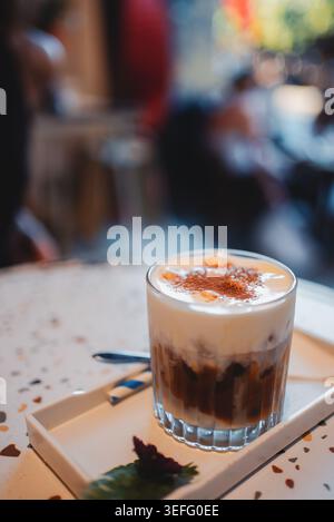 Eiskaffee Latte mit Creme-Schaum in gemütlichem Café, cremiges Kaltgetränk mit Zimt-Belag Stockfoto