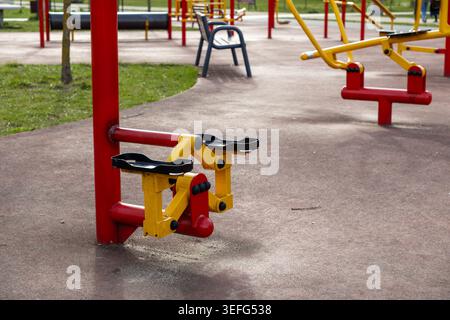 Ein Metallschritt-Trainingsgerät in einem öffentlichen Fitnessbereich im Freien bietet helle Primärfarben, um Herz-Kreislauf-Training und körperliches Wohlbefinden zu fördern Stockfoto