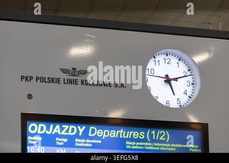 Warschau, Polen - 13. April 2026: Nahaufnahme einer PKP Polskie Linie Kolejowe Bahnhofsuhr mit digitaler Abfahrtstafel, die öffentliche Verkehrsmittel zeigt Stockfoto