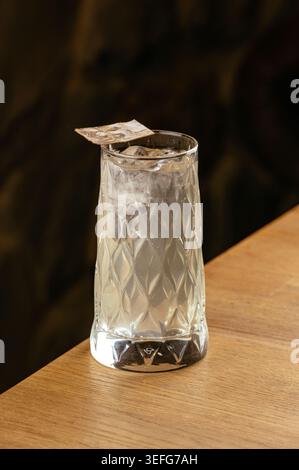 Eiskalter Craft-Cocktail in einem gemusterten Glas an einer Holzbar Stockfoto