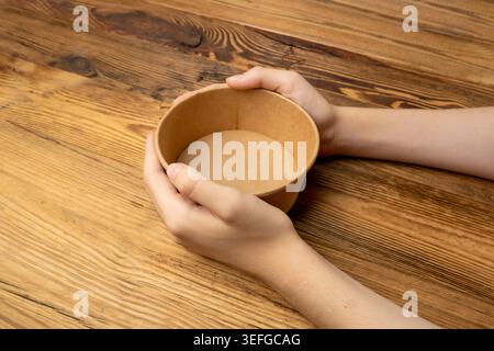 Schüssel in den Händen, leere Schüssel in den Armen auf hölzernem Hintergrund, Vintage Küchengeschirr Mockup, Geschirr Banner, Leere Platte, Hunger Konzept, Pape Stockfoto