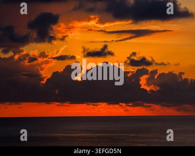 Luftaufnahme eines dramatischen Sonnenuntergangs über dem Indischen Ozean auf Mauritius Island mit dunklen Wolken, die von leuchtendem Orange- und Rotlicht beleuchtet werden, Moka District, Mau Stockfoto