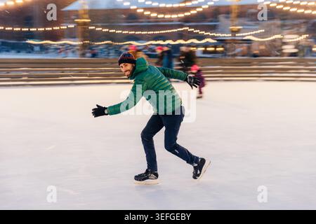 Ein Mann in Speed demonstriert seine Fähigkeiten im Skaten, hat Spaß am Ring, fühlt sich sicher und selbstbewusst auf dem Eis, verbringt Freizeit im Freien, genießt Winterferien, wird in Bewegung fotografiert Stockfoto