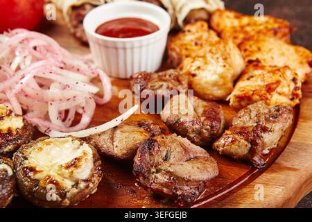 Verschiedene gegrillte Fleischgerichte, einschließlich Schaschlik mit Rindfleisch und Hühnchen mit Gemüse, Pilzen, eingelegten Zwiebeln und Lavash Wraps auf Holzbrett. Grillplatte mit Sauce, traditionelles Küchenkonzept. Stockfoto