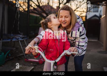 Mutter bekommt einen Kuss von ihrer glücklichen Tochter, während sie Fahrrad fahren lernt Stockfoto