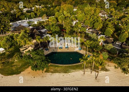 Blick aus der Vogelperspektive auf ein luxuriöses tropisches Resort mit einem dunklen Swimmingpool umgeben von Palmen und einem weißen Sandstrand Moka District, Mauritius. Stockfoto