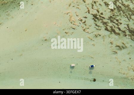 Blick aus der Vogelperspektive auf zwei kleine Boote, die in flachem türkisfarbenem Wasser über einem sandigen Meeresboden im Moka District, Mauritius, ankern. Stockfoto