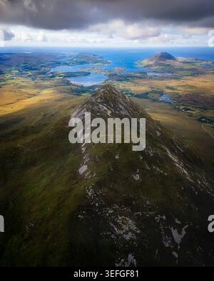 Blick aus der Vogelperspektive auf den Diamond Hill Peak mit Blick auf die zerklüftete Landschaft und die Küstenseen unter einem dramatischen bewölkten Himmel in County Galway, Irland. Stockfoto