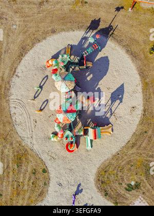 Blick aus der Vogelperspektive auf einen farbenfrohen Kinderspielplatz mit Rutschen und Kletterrahmen auf einer runden Sandgrube, umgeben von trockenem Gras in Turin, Piemont, Ita Stockfoto
