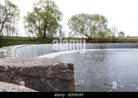 Ein künstlicher Wasserfall in einem Stadtpark. Eine Wasserkaskade mit Stufen im Stausee in der Nähe des Staudamms. Die Schönheit der Natur. Industrielle Architektur von Stockfoto