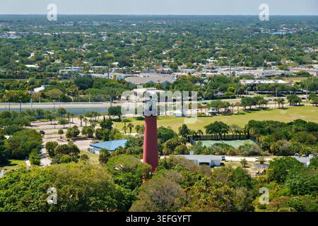 Blick aus der Vogelperspektive auf den roten Jupiter Inlet Lighthouse, umgeben von üppigen grünen Bäumen und einem Park mit Tennisplätzen in Jupiter, Florida, USA. Stockfoto