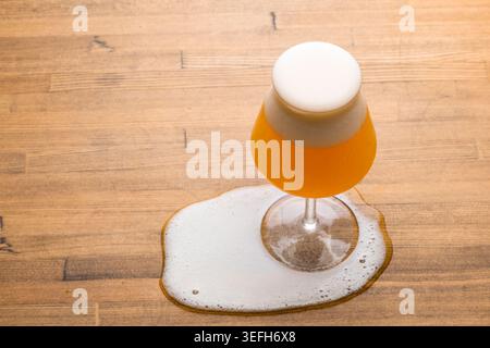 Ein Glas Bernsteinbier mit dickem Schaum, das auf einen Holztisch überfließt, von oben gesehen mit Kopierraum Stockfoto