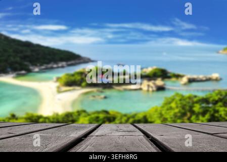 Premium-Hochwinkelansicht mit selektivem Fokus der Tischplatte aus dunklem Holz zur Produktpräsentation über dem unscharfen Aussichtspunkt der Insel Koh Nang Yuan und dem Strand Stockfoto