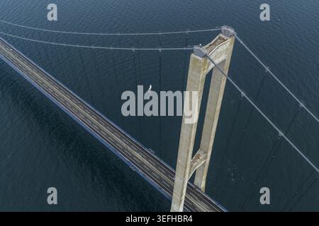 Aus der Vogelperspektive auf den Pylon der Great Belt Bridge und die Hängeseile über dem dunkelblauen Meer mit einem kleinen Segelboot unter Dänemark. Stockfoto