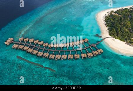 Blick aus der Vogelperspektive auf luxuriöse Bungalows über dem Wasser, die in einer gebogenen Linie über türkisfarbene Korallenriffe und einen weißen Sandstrand in Hoarafushi, Haa Alif Atoll, M angeordnet sind Stockfoto