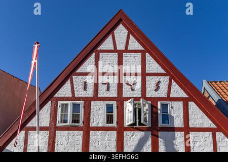 Blick auf einen traditionellen Fachwerkgiebel mit roten Balken und weißem Ziegelwerk unter einem klaren blauen Himmel in Ribe, Dänemark. Stockfoto