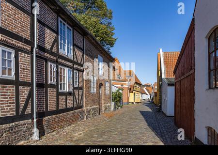 Blick auf historische Fachwerkhäuser entlang einer engen Kopfsteinpflasterstraße unter klarem blauen Himmel in der Altstadt von Ribe, Dänemark. Stockfoto