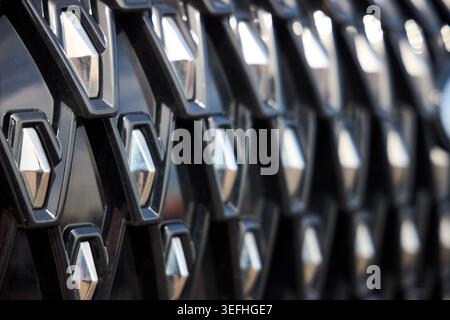 Nahaufnahme des komplexen Kühlergrills des Autos mit sich wiederholenden geometrischen Rautenmustern. Verchromte Elemente stehen im Kontrast zu dunkel strukturiertem B Stockfoto