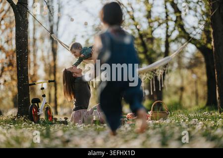 Mutter spielt mit ihren Kindern in einem sonnigen Park Picknick an einer Hängematte im Frühling Stockfoto