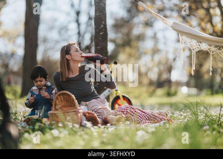 Mutter mit Kindern entspannt sich auf einer Picknickdecke in einem sonnigen Park und genießt Familienzeit Stockfoto