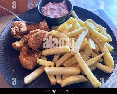 Goldene knusprige Hähnchennuggets serviert mit dickgeschnittenen Pommes frites und cremiger Dippsauce auf einem schwarzen Teller. Köstliches Fast Food. Stockfoto
