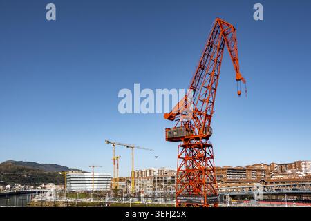Blick auf den berühmten roten Carola Crane im Itsasmuseum Bilbao mit urbanen Gebäuden und einem klaren blauen Himmel im Großraum Bilbao, Baskenland, Spanien. Stockfoto