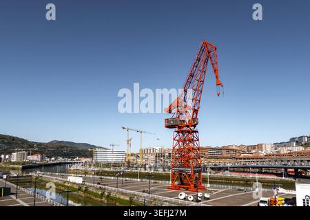Blick auf den berühmten roten Carola Crane am Ufer des Nervion River mit Stadtgebäuden und einem klaren blauen Himmel Greater Bilbao, Baskenland Stockfoto
