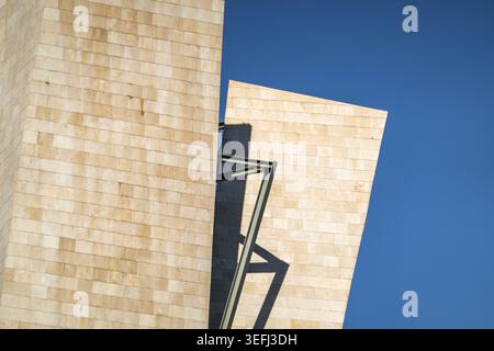Blick auf das Guggenheim Museum Bilbao mit modernen Kalksteinmauern und scharfen geometrischen Winkeln vor einem klaren blauen Himmel Bilbao, Euskadi, Spanien. Stockfoto