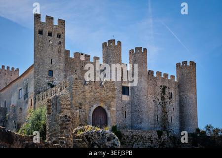 Flacher Blick auf die Burg Obidos in Obidos, Portugal, mit mittelalterlichen Steinmauern, runden Türmen und befestigten Toren unter einem hellblauen Himmel. Stockfoto