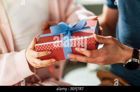 Herzerwärmendes Nahbild von zwei Personen, die eine wunderschön verpackte rote Geschenkbox mit einem blauen Band austauschen. Dieser berührende Moment fängt den Geist o ein Stockfoto