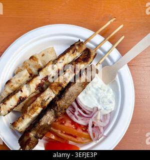 Authentische griechische Essensplatte mit Souvlaki-Spießen, Pitabrot, Tzatziki-Sauce, Tomaten und roten Zwiebeln auf einem Holztisch. Draufsicht. Stockfoto