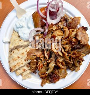 Authentische griechische Essensplatte mit Gyros-Fleisch, Pitabrot, Tzatziki-Sauce, Tomaten und roten Zwiebeln auf einem Holztisch. Draufsicht. Stockfoto
