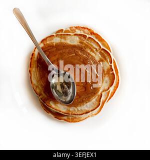 Blick von oben auf gestapelte amerikanische Pfannkuchen mit süßem Sirup und einem Stahllöffel. Leckeres Frühstück oder Brunch-Konzept. Saubere, minimalistische Lebensmittelfotografie. Stockfoto