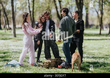 Gruppe junger Freunde lacht und umarmt in einem sonnigen Park mit Rucksäcken und einem Hund Stockfoto